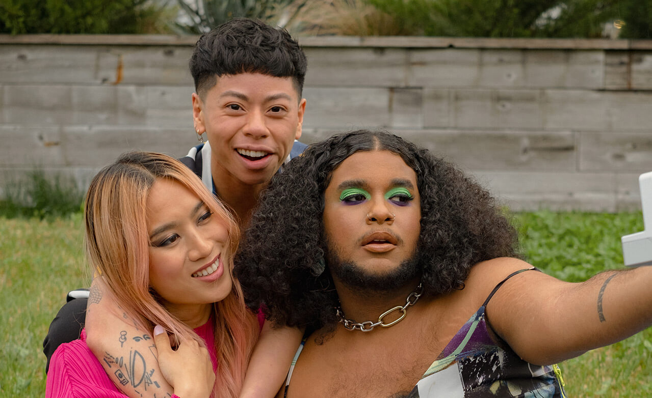 Three friends of varying genders taking a selfie in a park with a polaroid camera