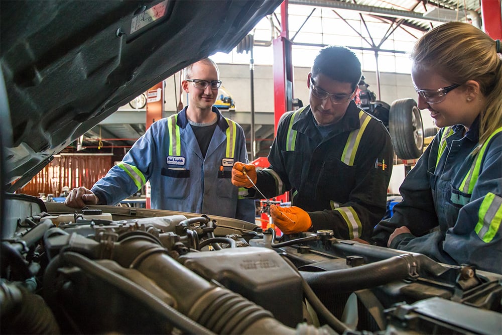 Students working on vehicle engine with instructor